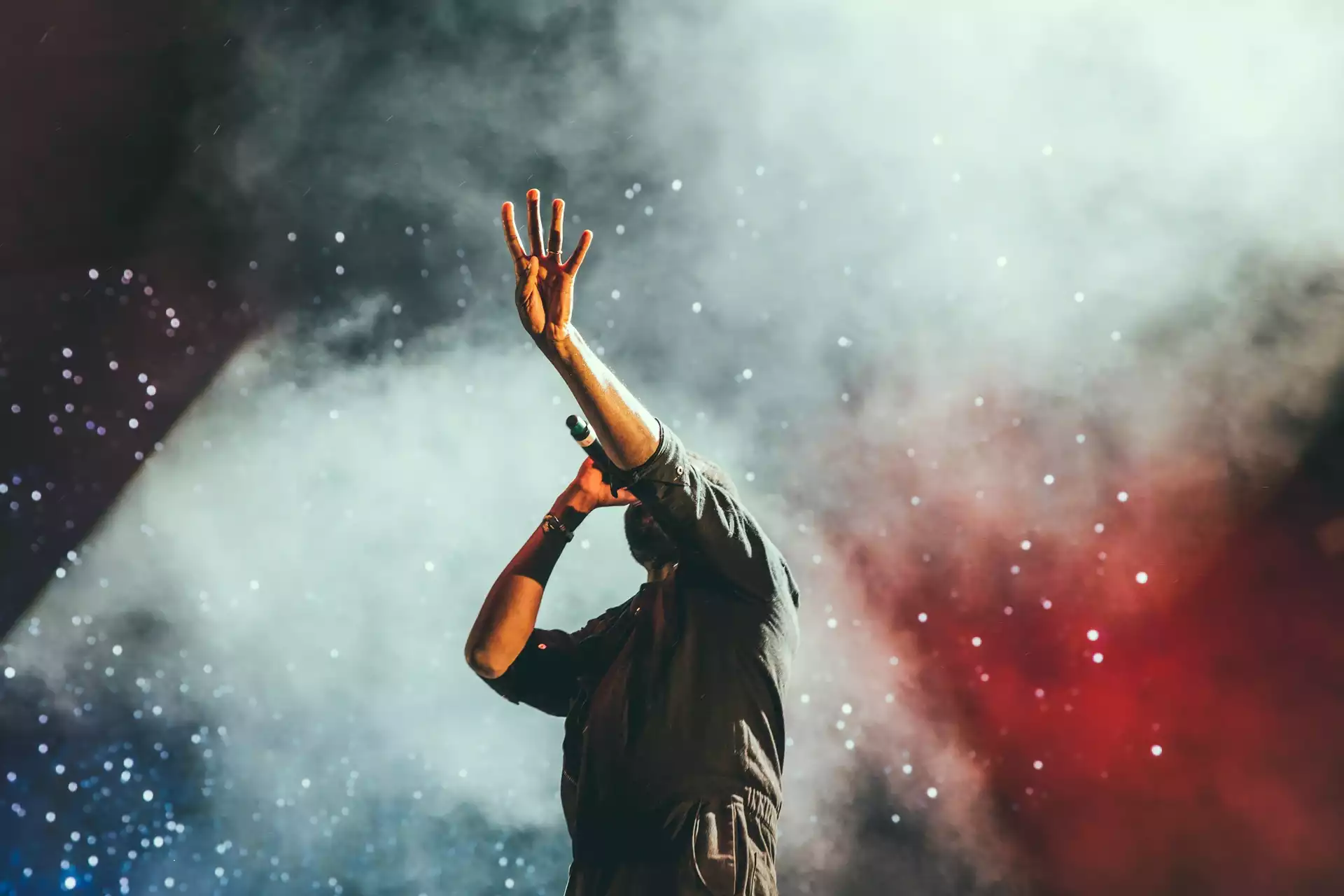Photo d'un chanteur lors d'un concert levant ses quatres doigts vers le ciel